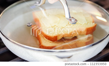 Within the sleek setting of a modern white kitchen, banana slices and brioche bread sizzle on a non-stick pan over a gas stove, setting the stage for an enticing grilled peanut butter banana sandwich. Within the sleek setting of a modern white kitchen, banana slices and brioche bread sizzle on a non-stick pan over a gas stove, setting the stage for an enticing grilled peanut butter banana sandwich. 112353950