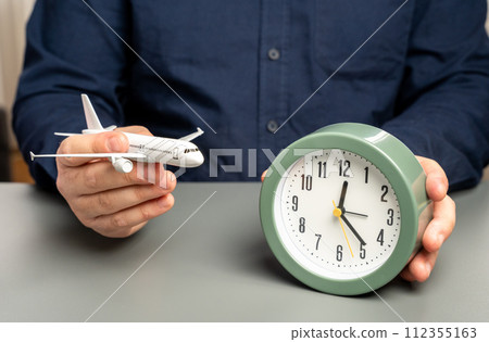 A man holds a passenger plane and a clock. Flight time. Planning a route with transfers. 112355163