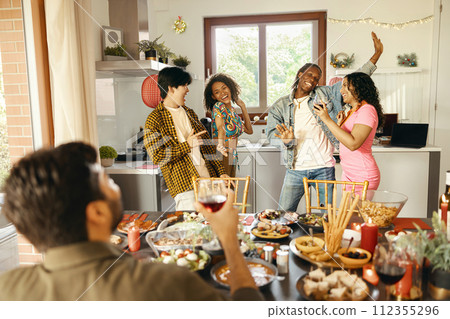 Cheerful young group of diverse friends holding drinks and dancing at home kitchen during party time Cheerful young group of diverse friends holding drinks and dancing at home kitchen during party time 112355296