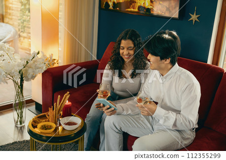 Positive friends drink wine and looking on phone during holiday party at home. High quality photo 112355299