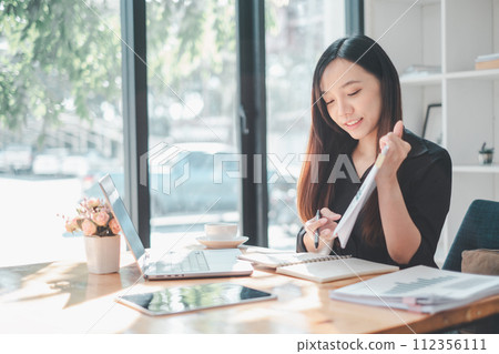A focused young woman meticulously reviews documents, surrounded by her organized workspace bathed in sunlight, symbolizing productivity and careful planning. A focused young woman meticulously reviews documents, surrounded by her organized workspace bathed in sunlight, symbolizing productivity and careful planning. 112356111