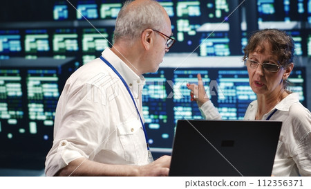 Older colleagues looking around innovative server farm, preparing to start comission on malfunctioning high tech establishment hardware rows in order to ensure perfect operations 112356371