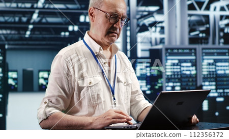 Trained engineer expertly managing data while navigating in industrial server room. Specialist ensuring errorless cybersecurity protection, optimizing systems and performing necessary updates 112356372