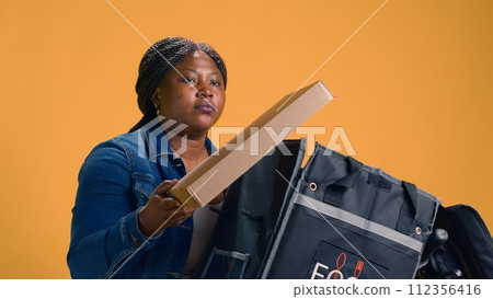 Healthy black woman on bicycle delivering fresh pizza order from local restaurant. African american delivery person providing exceptional customer service with takeaway delivery. Healthy black woman on bicycle delivering fresh pizza order from local restaurant. African american delivery person providing exceptional customer service with takeaway delivery. 112356416
