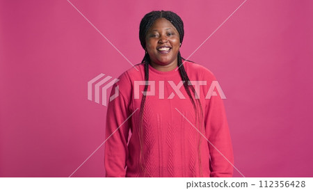 Stunning african american lady in pink stylish outfit laughing for camera at photo shoot. Vibrant female fashionista model chuckling against pink background. Slow-mo, portrait shot. 112356428