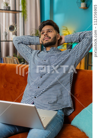 Young man freelancer sitting on couch close laptop pc after finishing work in living room at home 112356905