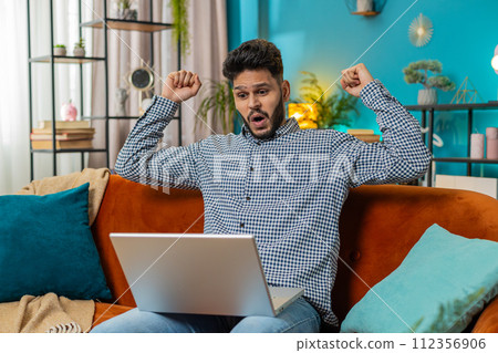Amazed Indian man use laptop computer, receive good news message shocked by victory, celebrate win 112356906
