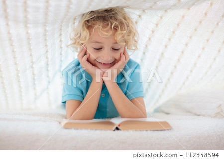 Child reading book in bed. Kids read books. 112358594
