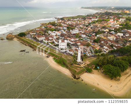 Aerial view of Galle lighthouse and Galle fort walls in the Bay of Galle on the southwest coast of Sri Lanka. Galle Fort is one of a cultural heritage of UNESCO World Heritage Site in Sri Lanka. Aerial view of Galle lighthouse and Galle fort walls in the Bay of Galle on the southwest coast of Sri Lanka. Galle Fort is one of a cultural heritage of UNESCO World Heritage Site in Sri Lanka. 112359835