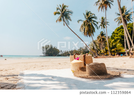 Beach and tropical paradise with a coconut resting on the sand and a refreshing coconut cocktail nearby beneath swaying palm trees 112359864