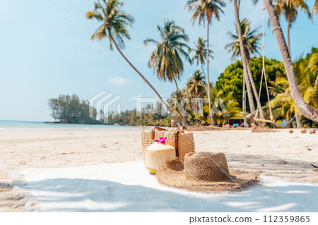Beach and tropical paradise with a coconut resting on the sand and a refreshing coconut cocktail nearby beneath swaying palm trees 112359865