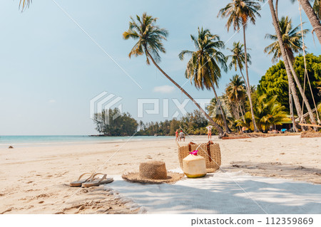 Beach and tropical paradise with a coconut resting on the sand and a refreshing coconut cocktail nearby beneath swaying palm trees 112359869