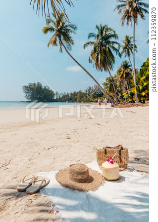 Beach and tropical paradise with a coconut resting on the sand and a refreshing coconut cocktail nearby beneath swaying palm trees 112359870