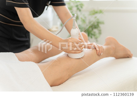 An esthetician and a man (legs) performing slimming esthetics using a cavitation esthetics machine at a men's esthetician An esthetician and a man (legs) performing slimming esthetics using a cavitation esthetics machine at a men's esthetician 112360139