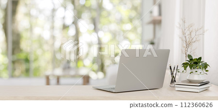 A back view image of a laptop on a wooden desk in a minimalist bright living room. 112360626