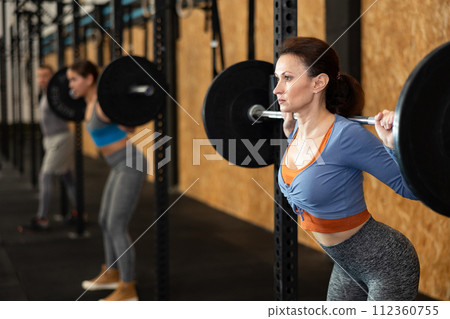 Caucasian woman training with barbell using squat rack in crossfit gym Caucasian woman training with barbell using squat rack in crossfit gym 112360755