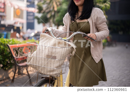 A cropped shot of a woman pushing her bicycle on the street in the city. 112360981