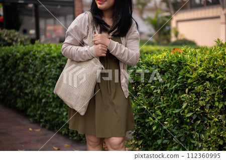 A cropped shot of a happy Asian woman in casual clothes walking in the city. 112360995