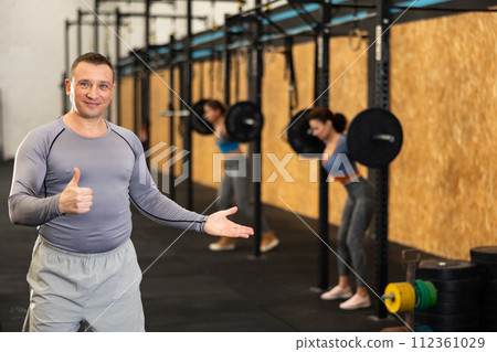 Positive middle-aged trainer with thumbs-up gesture in gym 112361029