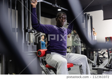 African american man is engaged in a simulator for development of back muscles 112361072