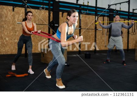 Female trainer helping girl to train with resistance band in sport gym 112361131