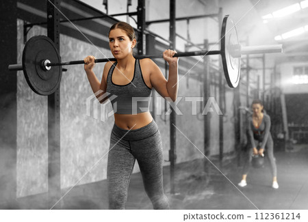 Caucasian woman training with barbell using squat rack in crossfit gym 112361214