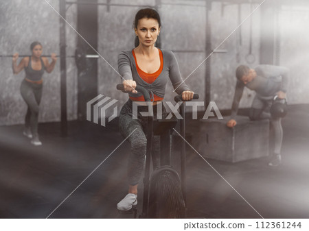 Middle-aged woman doing cardio workout on stationary bicycle ellipsoid. Functional training concept 112361244