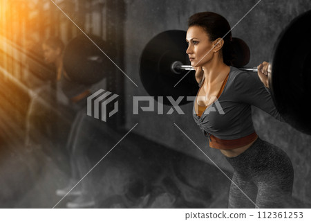Slender woman trains muscles of arms and back using barbell and differentiated weighting in gym 112361253