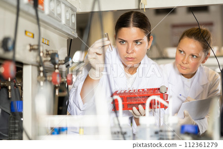 Adult and young female chemists examine liquid in beaker in laboratory Adult and young female chemists examine liquid in beaker in laboratory 112361279