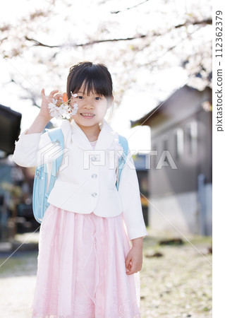 A girl who entered elementary school with a school bag on her back stands with a smile under a cherry tree A girl who entered elementary school with a school bag on her back stands with a smile under a cherry tree 112362379