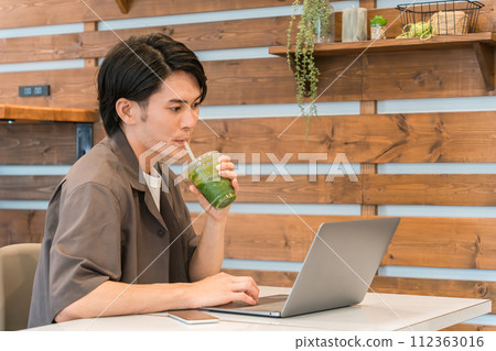 一名男子在電腦前工作時透過喝綠色冰沙、綠色果汁和蔬菜汁來禁食和節食 112363016