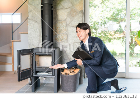 A male house builder businessman in a suit explaining how to use a wood stove 112363138