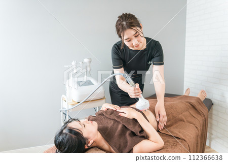 Esthetician/therapist and woman performing slimming beauty treatment using cavitation machine at beauty salon 112366638