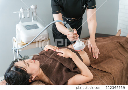 Esthetician and woman performing slimming beauty treatment using cavitation beauty machine at beauty salon 112366639