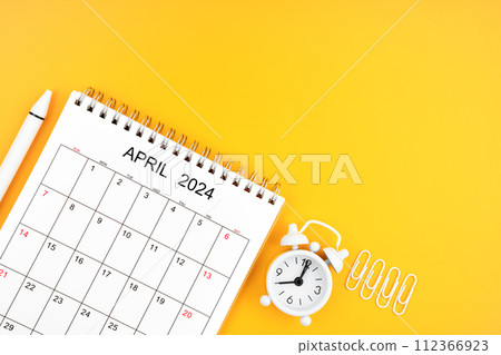April 2024, Monthly desk calendar for 2024 year and alarm clock with paper clips on yellow. April 2024, Monthly desk calendar for 2024 year and alarm clock with paper clips on yellow. 112366923