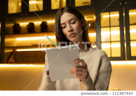 Young Woman Wearing a White Sweater Writing in a Notebook Young Woman Wearing a White Sweater Writing in a Notebook 112367443