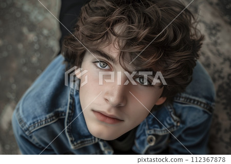 A young man with brown hair and blue jeans is sitting on the ground 112367878