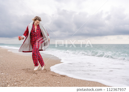 Lady in plaid shirt holding a gift in his hands enjoys beach with Christmas tree. Coastal area. Christmas, New Year holidays concep Lady in plaid shirt holding a gift in his hands enjoys beach with Christmas tree. Coastal area. Christmas, New Year holidays concep 112367937