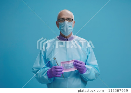 A man in a blue lab coat holding a dental instrument 112367939