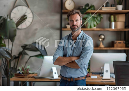 A man stands in front of a desk with two computer monitors and a clock 112367965