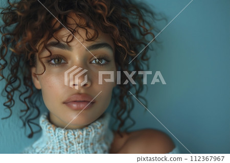 A woman with curly hair and a white sweater is standing in front of a blue wall A woman with curly hair and a white sweater is standing in front of a blue wall 112367967