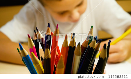A boy of 5-6 years old draws with pencils on paper. In the foreground is a glass with pencils. A boy of 5-6 years old draws with pencils on paper. In the foreground is a glass with pencils. 112368211