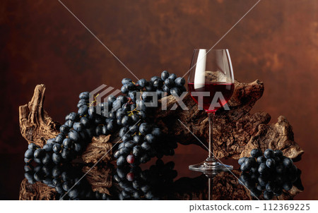 Glass of red wine with an old snag and blue grapes. Glass of red wine with an old snag and blue grapes. 112369225
