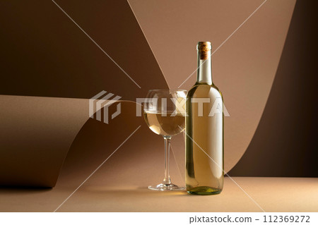 Bottle and glass of white wine on a beige background. 112369272