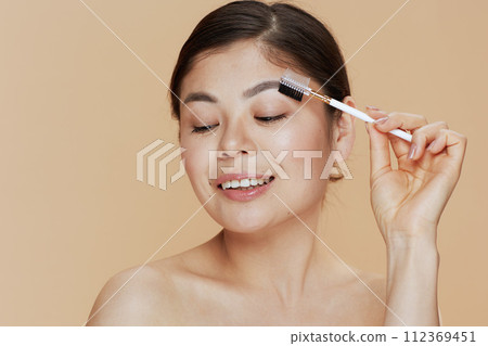 young asian woman with brow brush on beige background 112369451