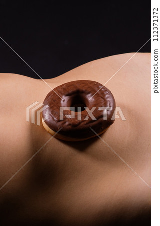 Close up shot of nude woman's body with a chocolate covered donuts Close up shot of nude woman's body with a chocolate covered donuts 112371372
