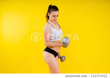 Sporty female doing exercise with dumbbells, silhouette studio shot dark yellow background Sporty female doing exercise with dumbbells, silhouette studio shot dark yellow background 112371412