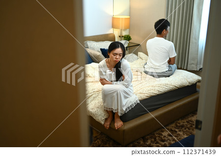 Serious young woman sitting on bed with boyfriend in background. Relationship difficulties conflict concept 112371439