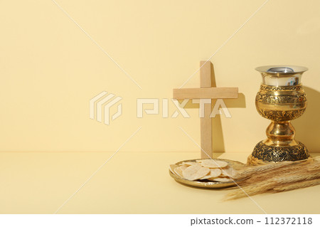 Wooden cross, liturgical bread, spikelets and cup on light background, space for text 112372118