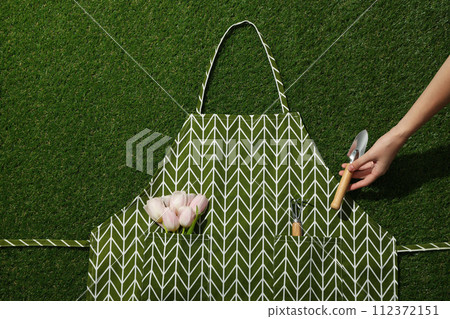Gardening tools and tulips in apron, hand on green background, top view 112372151